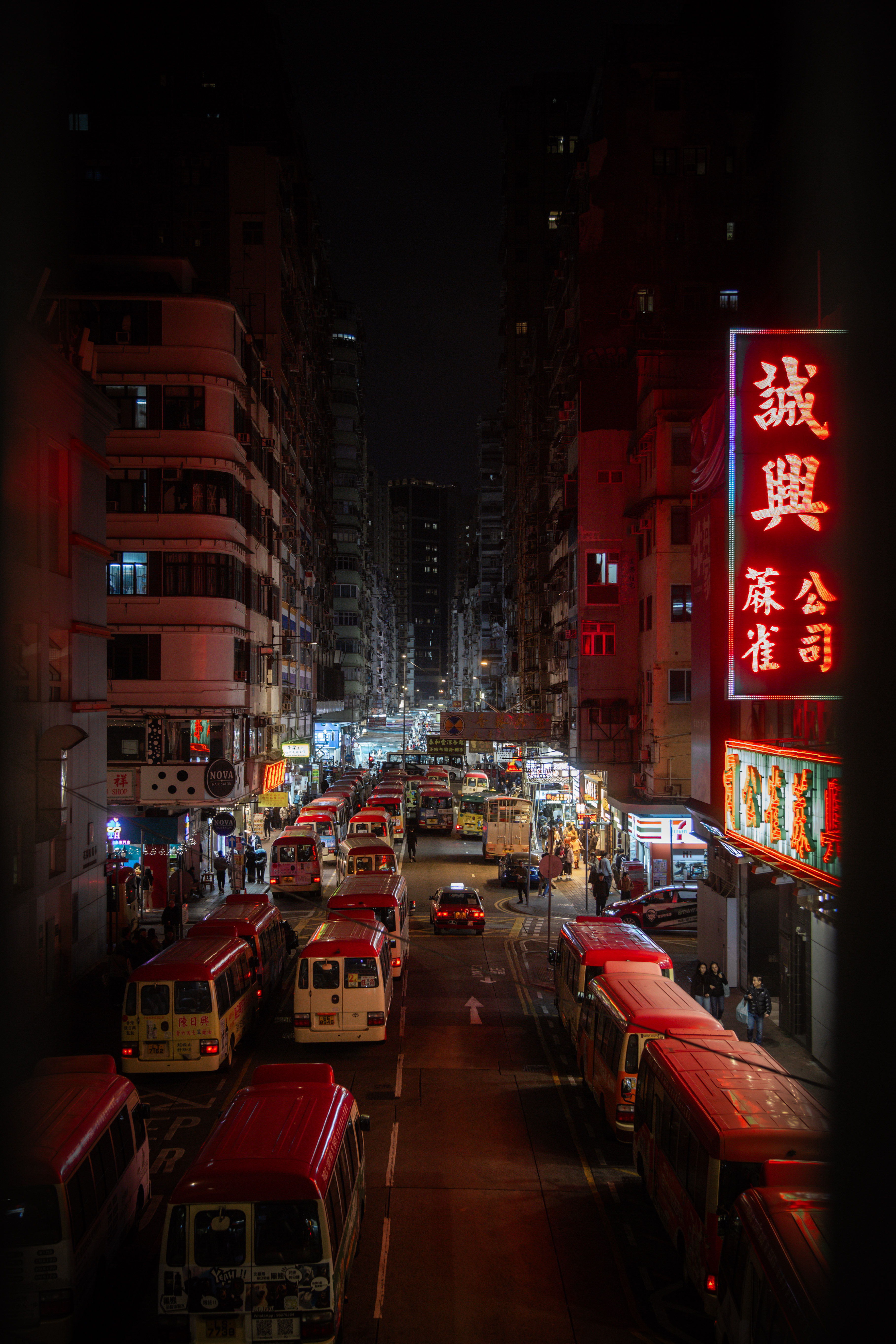 Red minibuses lined along a Mong Kok street at night